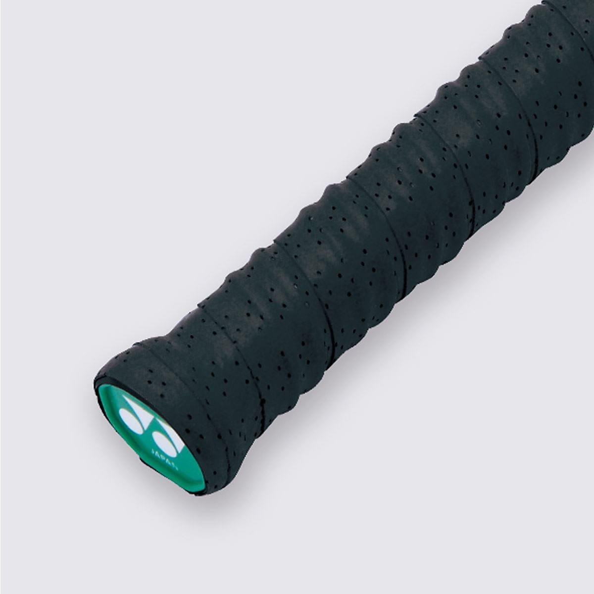 Close-up of a black tennis racket handle featuring a Yonex AC139EX Twin Wave Grap Badminton Overgrip, offering a tacky feel. The circular end displays a green sticker, adding a touch of vibrancy against the plain white background.