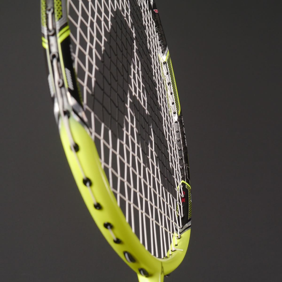 Close-up of the Ashaway Phantom X Speed II badminton racket, showcasing its advanced airflow system, with vibrant yellow and black accents against a dark background. The strings create a grid pattern that complements its sleek, modern design.