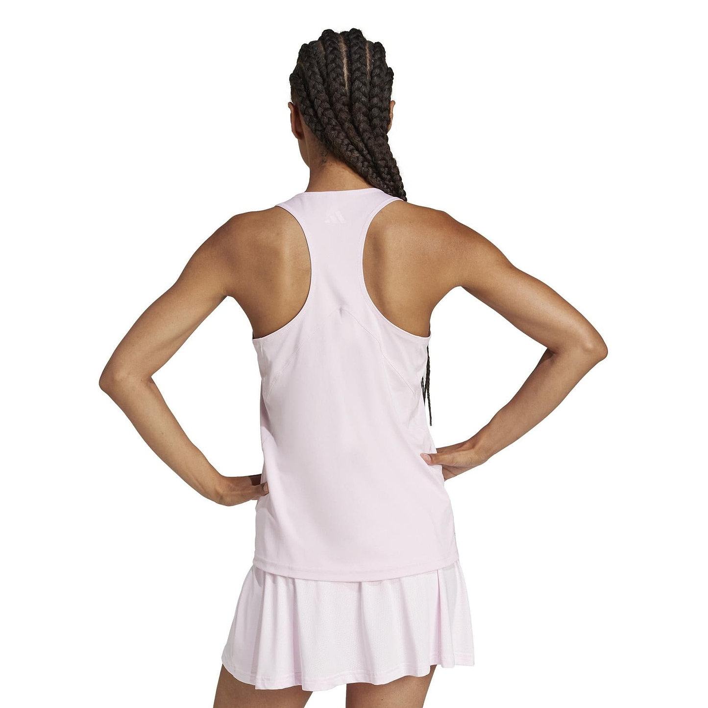 With her back to the camera, a person with long braided hair wears an adidas Women's Club Badminton Tank Top in pink and a matching pleated skirt made from recycled materials, hands on hips against a plain white background.