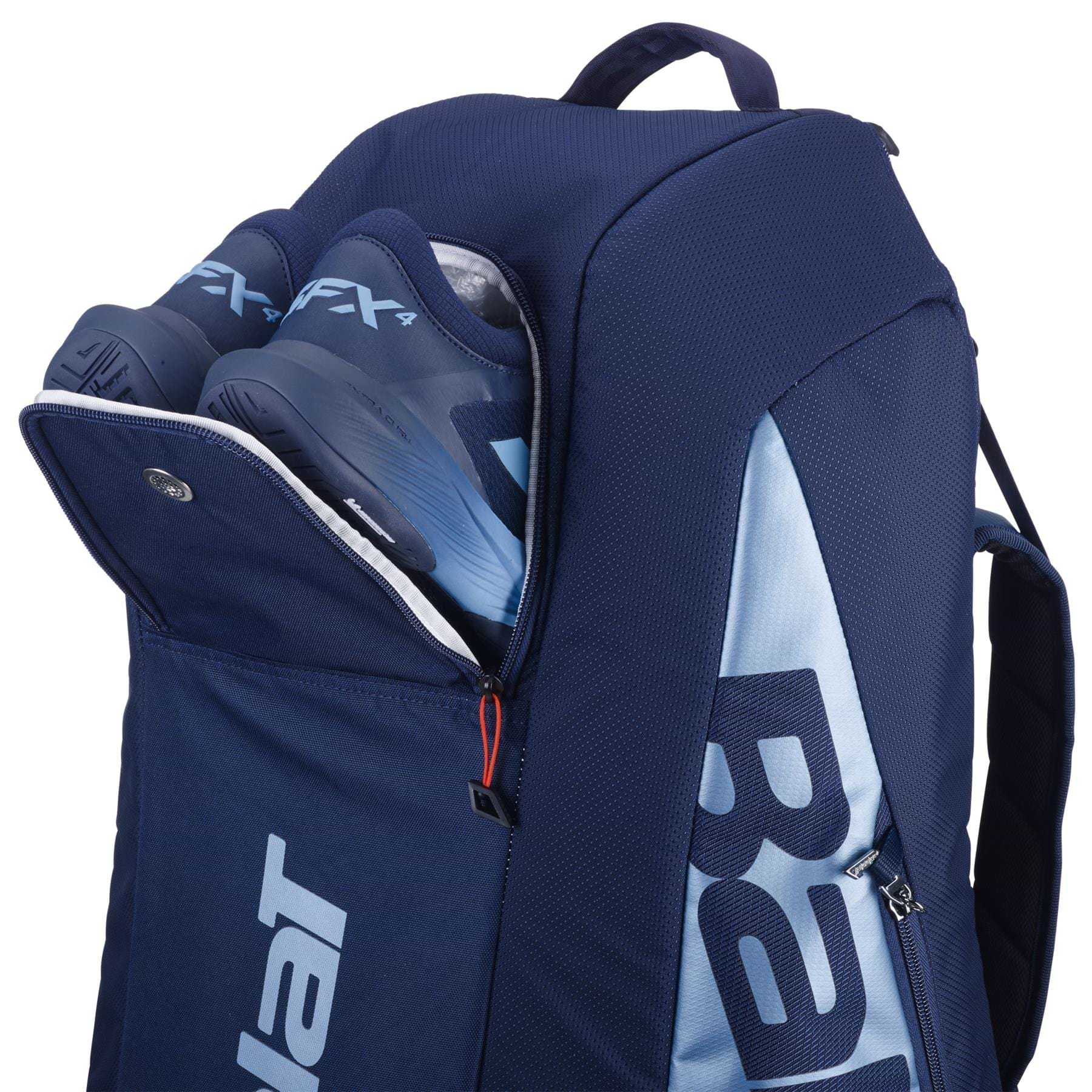 The Babolat RH6 Pure Drive Gen11 in navy blue, made from recycled polyester, shows two blue sports shoes inside its partially open pocket. It features a large zipper and white brand lettering on the side, resembling a sleek badminton racket bag.