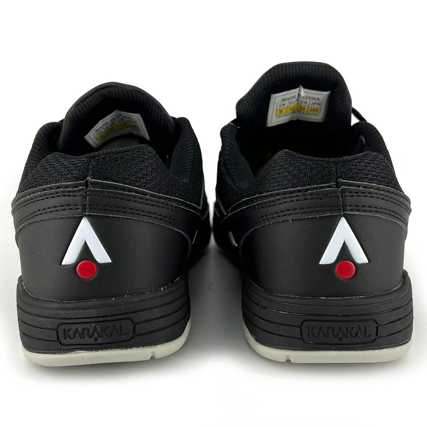 The image showcases the rear view of Karakal KF Pro Lite Badminton Shoes - New Black, highlighting black uppers paired with gray soles. The heels feature a white and red triangular logo, along with "Karakal" embossed on them, ensuring lateral stability and incorporating an advanced shock-absorbing gel insole to boost performance.