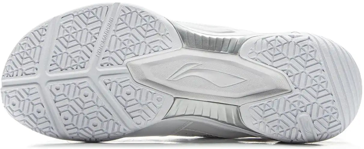 The image shows the outsole of the Li-Ning Sonic Boom Unisex Badminton Shoes in white, featuring a textured geometric tread, grooves for stability and protection, and a central Li-Ning logo—ideal for indoor court play.