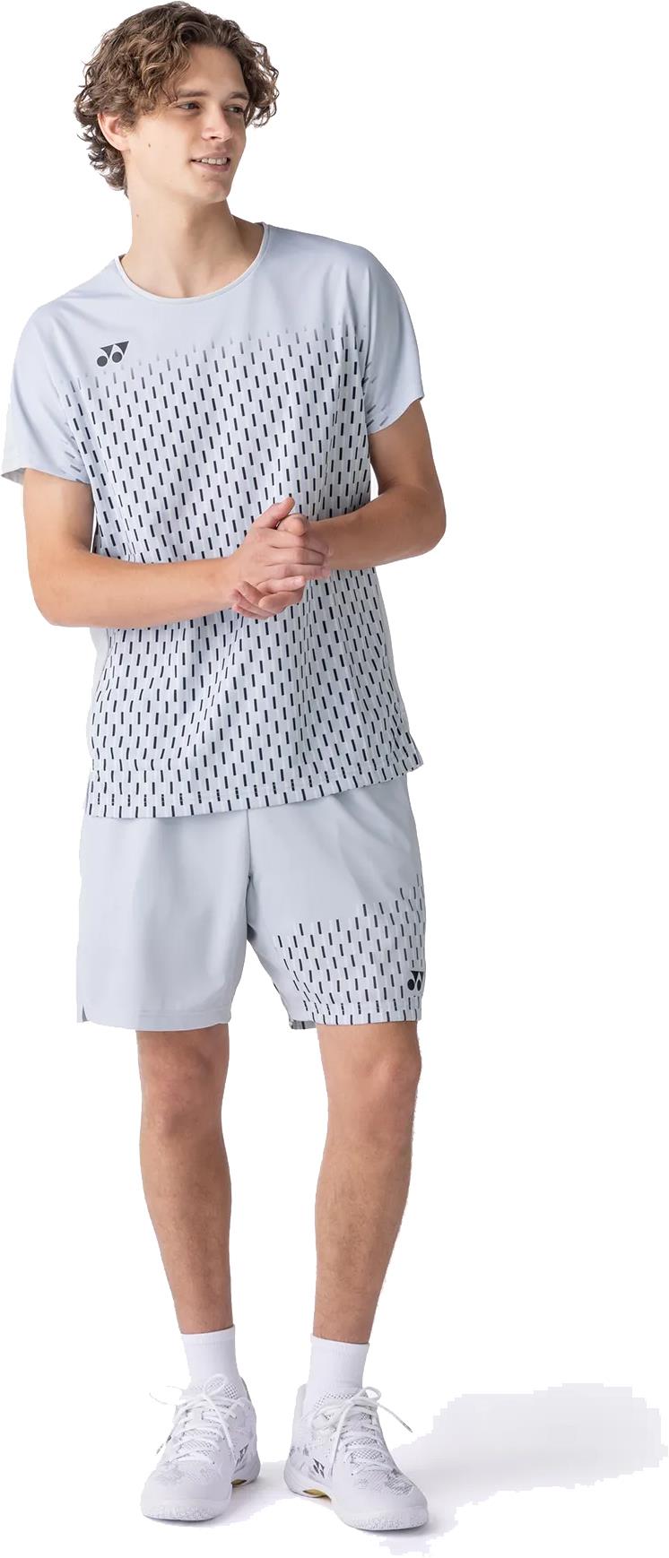 A young man wears the Yonex 10713EX Crew Neck Men's Badminton T-Shirt in Silver Grey, featuring a black dashed pattern. The moisture-wicking Yonex shirt keeps him cool as he looks to the side with hands loosely clasped.