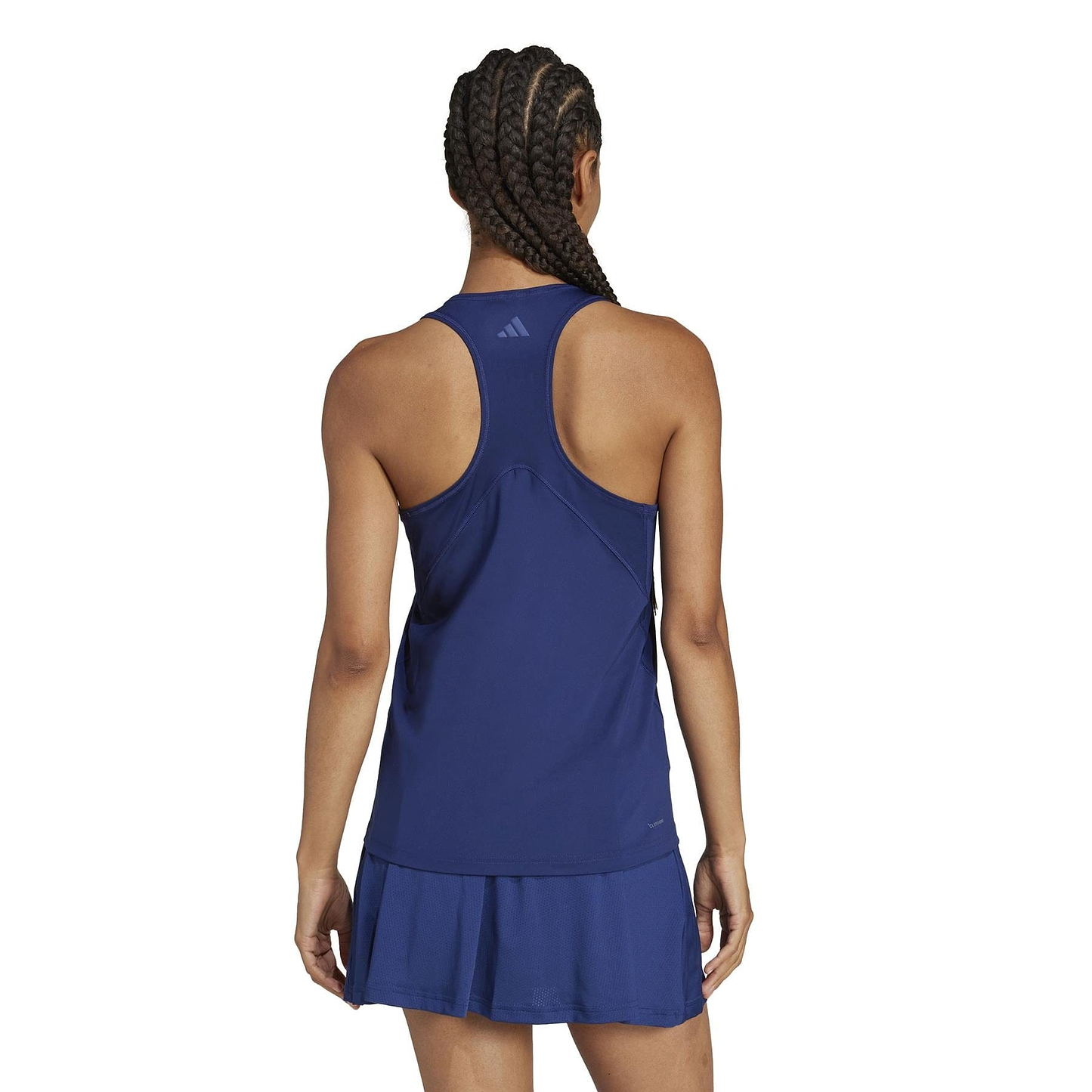 The individual with braided hair is seen from behind wearing a sleeveless, navy tennis dress made of recycled materials, featuring a racerback and pleated skirt similar to the ADIDAS Women's Club Badminton Tank Top by adidas.