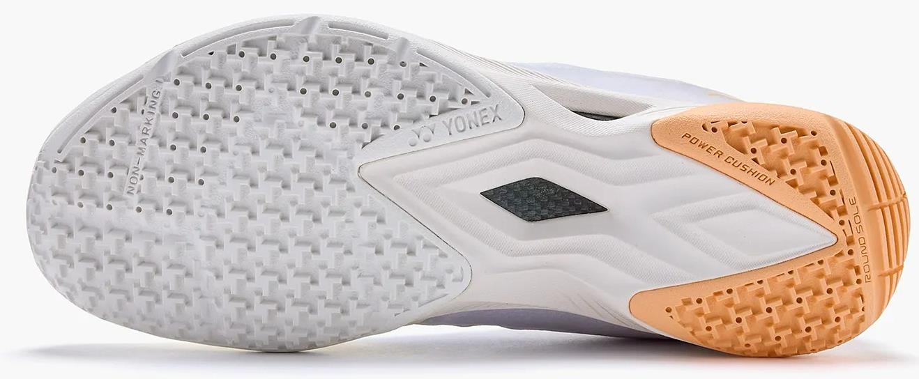 The image shows the sole of Yonex Power Cushion Aerus Z2 Womens Badminton Shoes in white and orange, with a textured grip pattern and visible "POWER CUSHION" text, designed specifically for women’s badminton.
