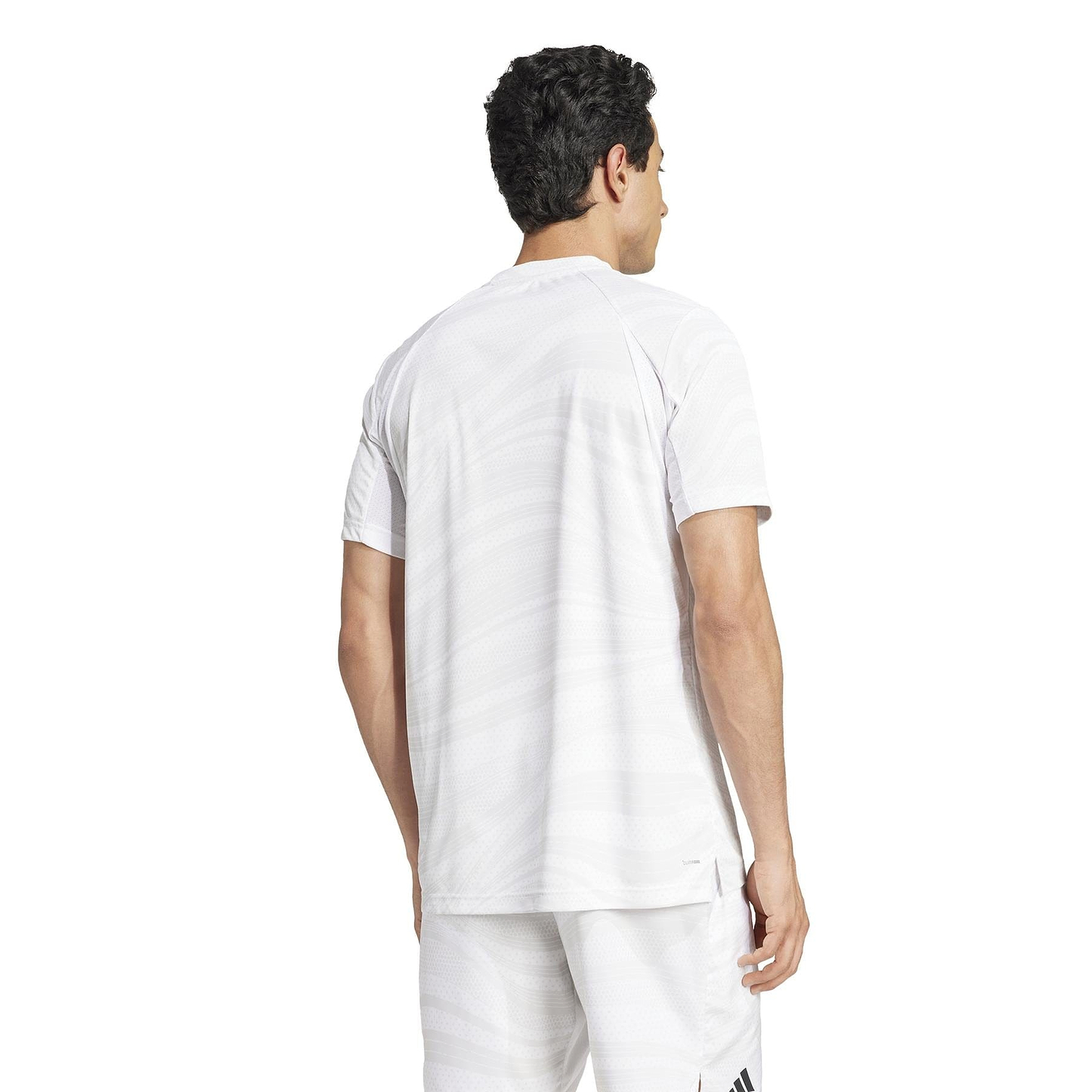 A man in an adidas Mens Club Graphic Badminton T-Shirt in white/grey and matching recycled-material shorts stands with his back to the camera against a plain white background.