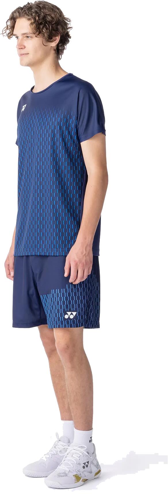A young man wears the Yonex 10713EX Crew Neck Men's Badminton T-Shirt in dark navy, featuring advanced moisture management technology, paired with matching navy shorts, white socks, and white sneakers.
