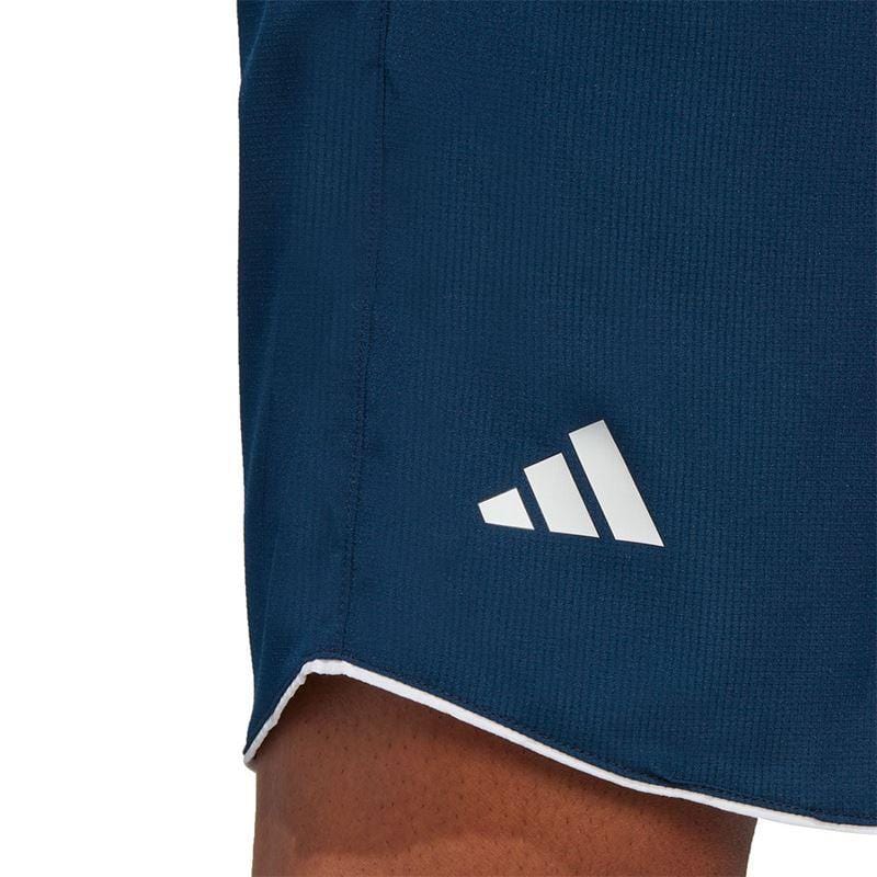 Close-up of a person wearing the navy ADIDAS Mens Club 7" Badminton Shorts by adidas, showcasing the distinctive white Adidas logo. The fabric, enhanced with AEROREADY technology, provides comfort and breathability. The edge of the shorts is tastefully detailed with a white trim.