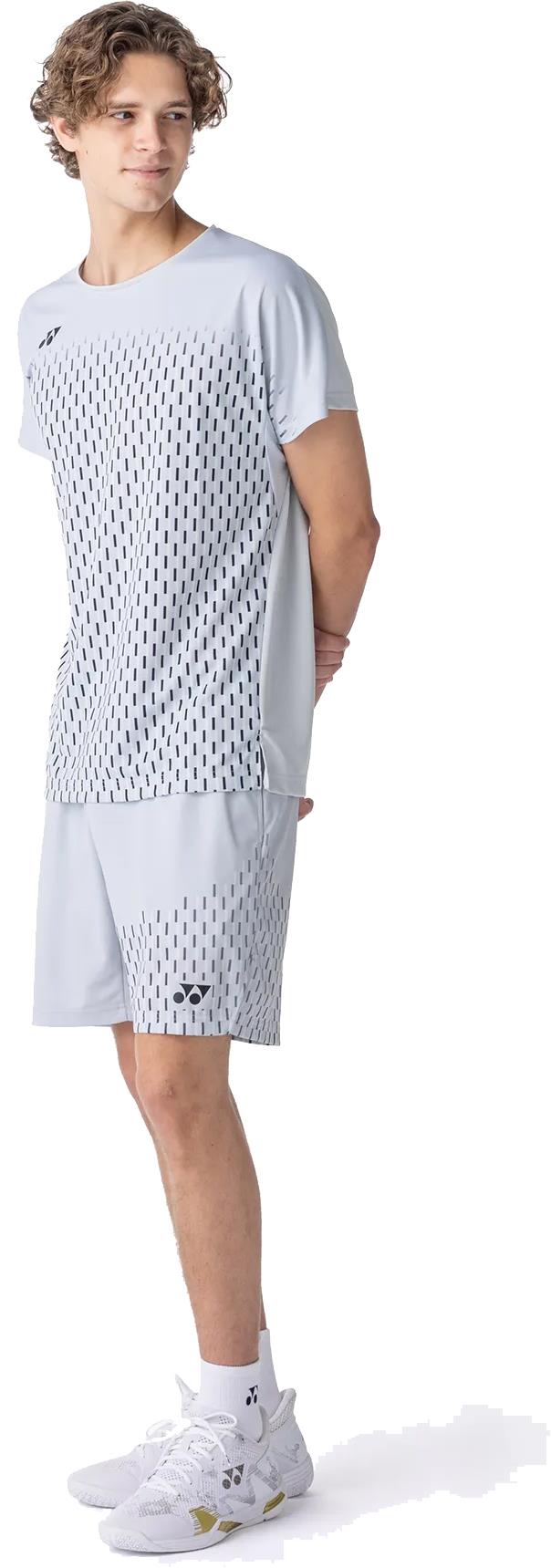 A young person stands sideways, wearing a Yonex 10713EX Crew Neck Mens Badminton T-Shirt in silver grey with black dotted patterns, matching shorts, white socks, and white athletic shoes against a white background.