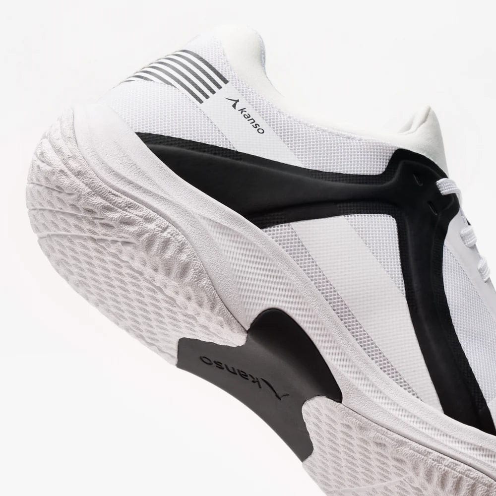 The Kanso Equilibrium EQx3 Unisex Badminton Shoes in white and black showcase a textured sole and layered design. "Kanso" is printed on the side, with geometric black accents, striped details on a white background, and Speedlight Foam for shock absorption, enhancing agility.