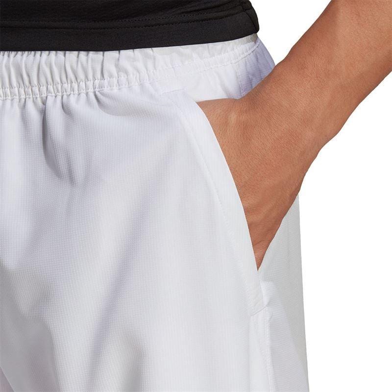 A person wearing Adidas Men's Club 7" Badminton Shorts in white, designed with AEROREADY technology, stands with a hand in the pocket against a plain background.