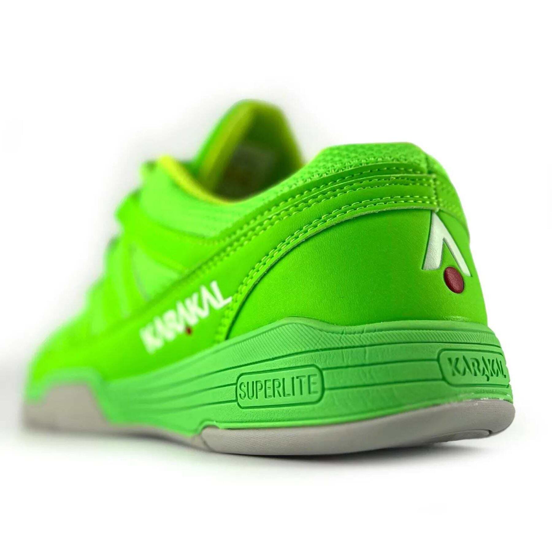The Karakal KF Pro Lite Badminton Shoes in vibrant green, ideal for badminton enthusiasts, feature a sleek Superlite design that enhances lateral stability. With a textured sole and visible stitching, the shoes are adorned with a distinctive white and red logo on the heel, angled to highlight both the back and side.
