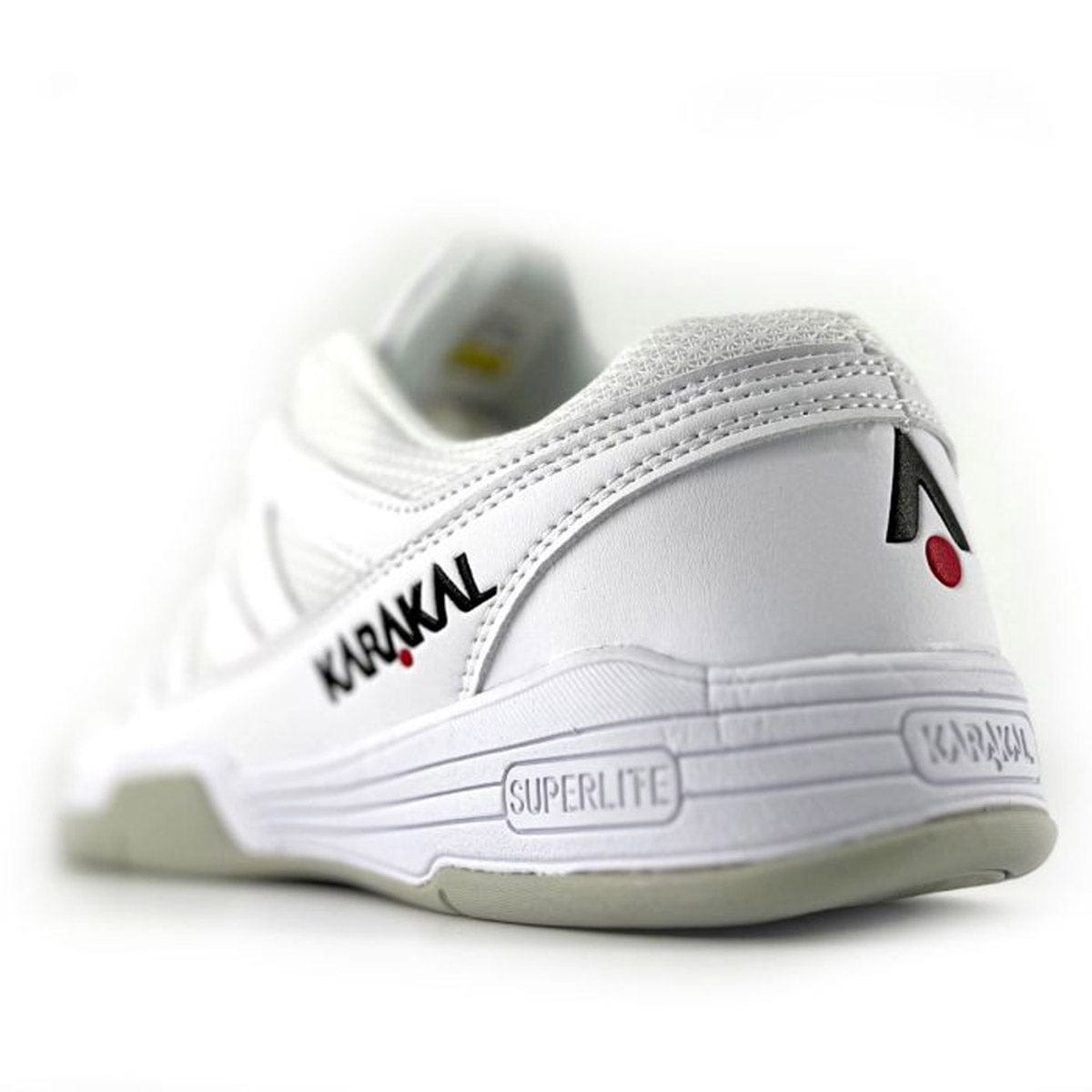 From the rear view, the Karakal KF Pro Lite Badminton Shoes in white display the brand name "Karakal" and "Superlite" on a gray sole. This performance-oriented shoe is equipped with a shock-absorbing gel insole, offers lateral stability, and boasts a sleek design accentuated by a red dot near the logo.
