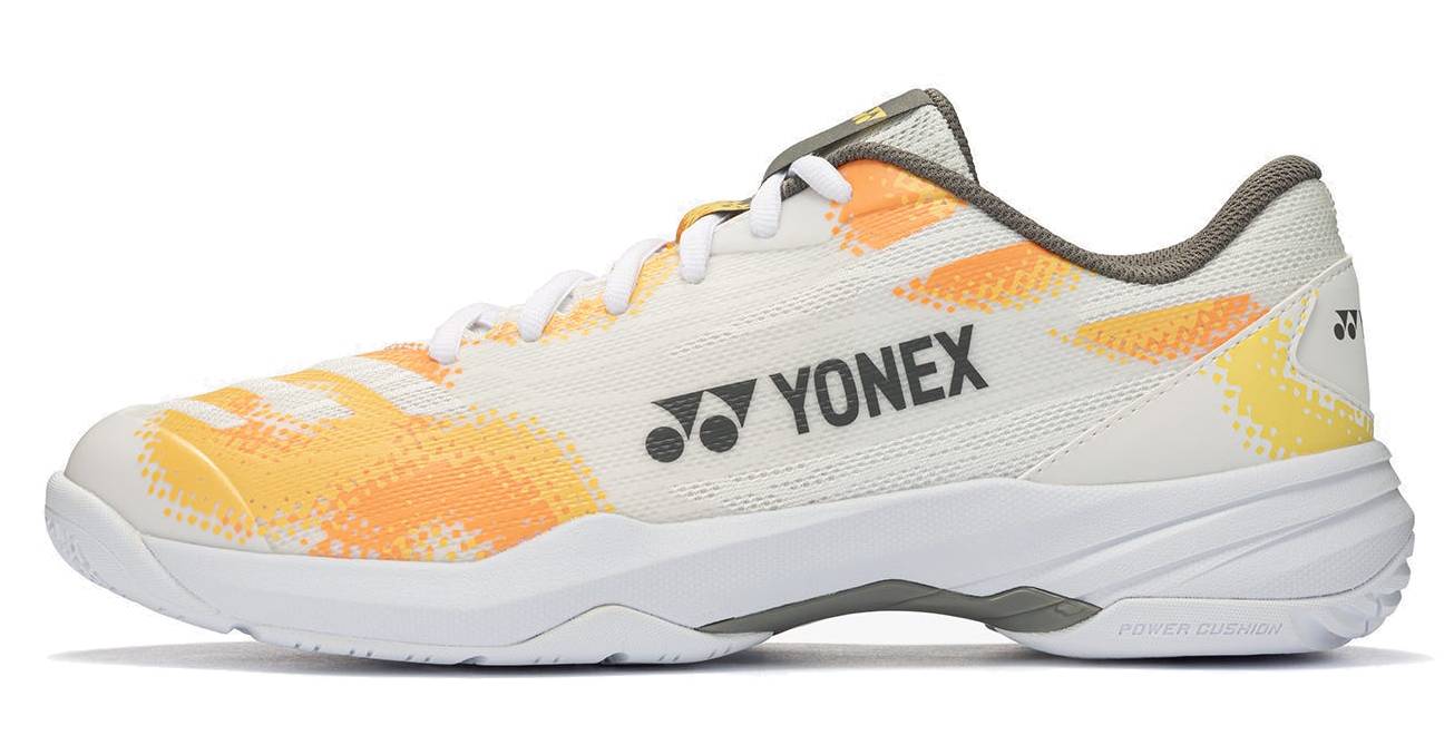 The Yonex Power Cushion Cascade Accel Unisex Badminton Shoes—White / Orange feature a white sole, a striking yellow-orange pattern, and “YONEX” branding on the side. Designed for intermediate players, these shoes come with white laces and incorporate advanced Yonex Power Cushion technology to provide enhanced comfort and support.