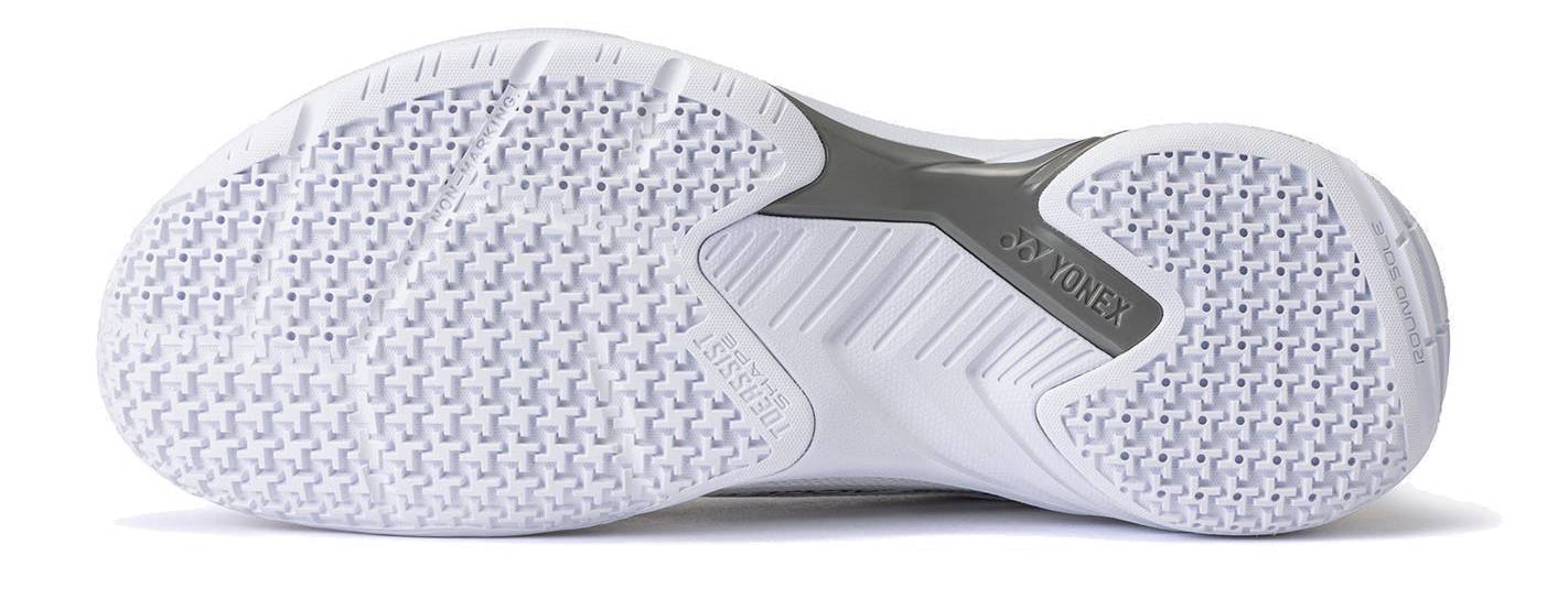 The image shows the white textured sole of the Yonex Power Cushion Cascade Accel Unisex Badminton Shoes in White / Orange, featuring intricate grip patterns and a gray support section in the middle—an excellent choice for players seeking an intermediate model with reliable Yonex Power Cushion technology.