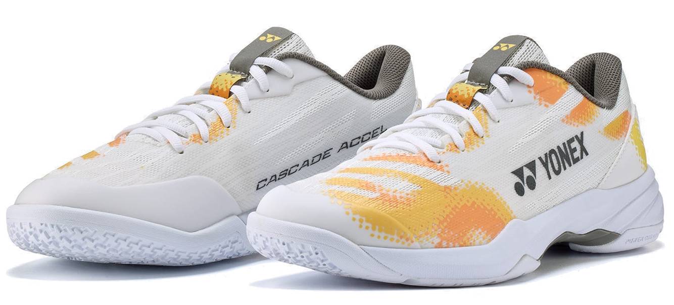A pair of Yonex Power Cushion Cascade Accel Unisex Badminton Shoes in white and orange, featuring gray laces, textured white soles with renowned Yonex Power Cushion technology, and positioned side by side as an ideal choice for intermediate players.