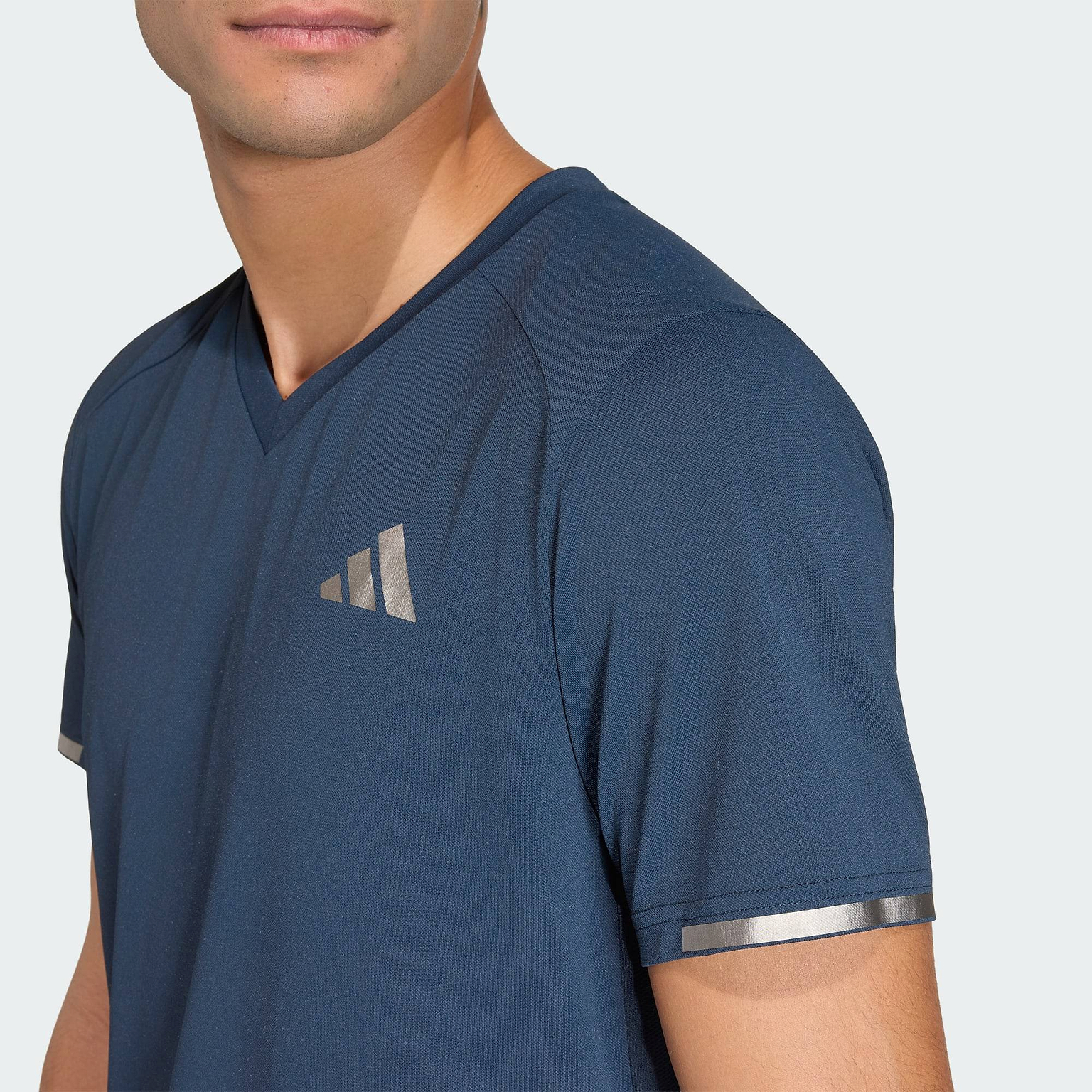 A person wears the ADIDAS Climacool+ Freelift Pro Mens Badminton T-Shirt - Aurora Ink by adidas, a blue V-neck with metallic silver accents and advanced cooling, against a plain light background.