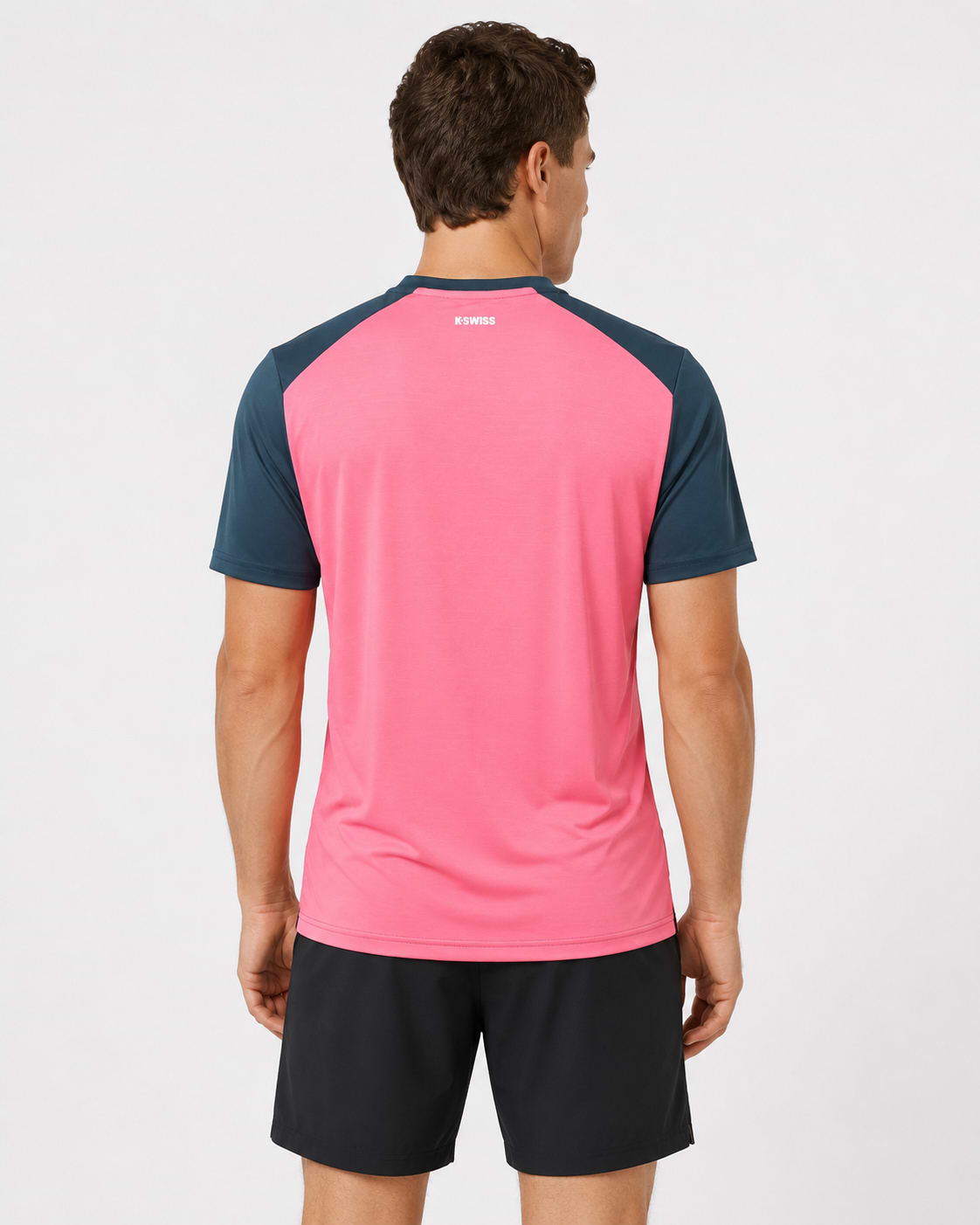 A man faces away from the camera, wearing a K-Swiss Hypercourt Mix Melange Men's Badminton T-Shirt in Stargazer/Pink and black shorts, against a plain white background.