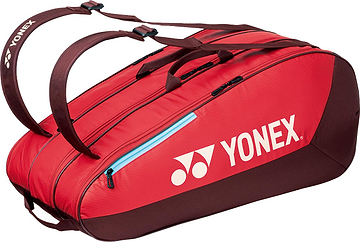 The Yonex 42529EX Team 9 Racket Badminton Bag in Ruby Red features brown handles, black zippers, the white Yonex logo, and multiple compartments for carrying sports gear.