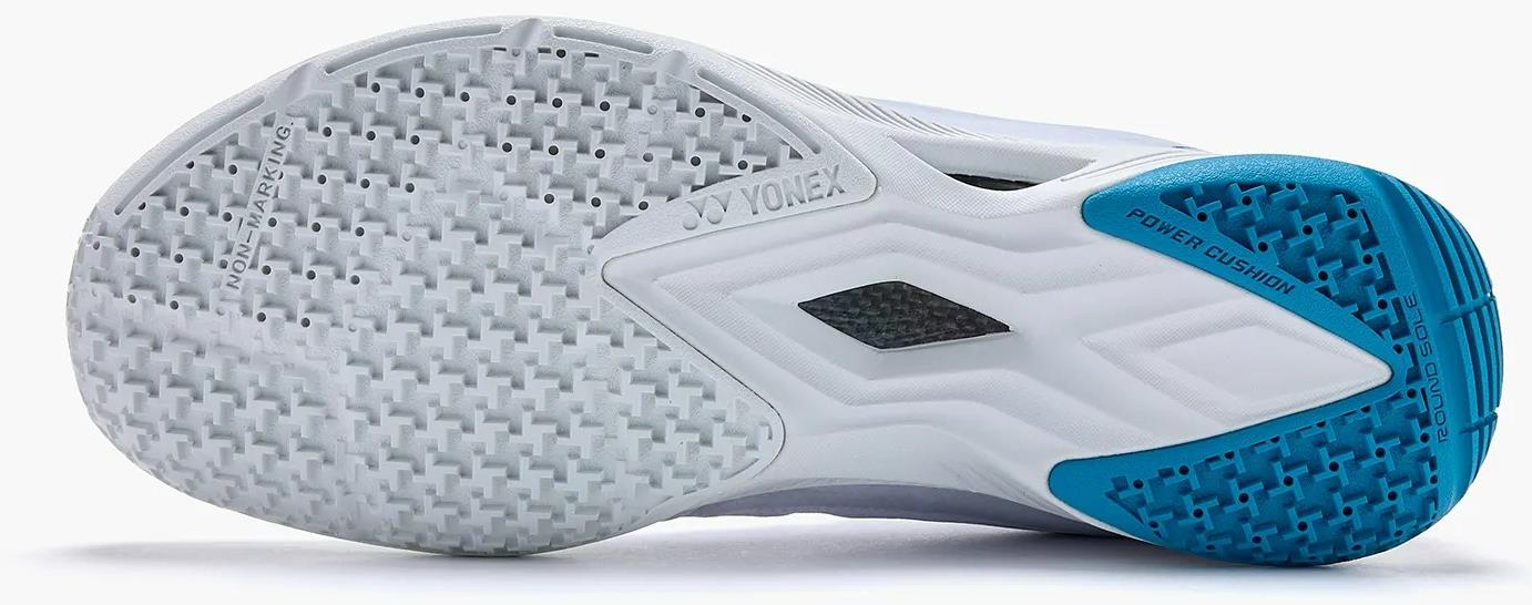 Close-up of the white sole on the Yonex Power Cushion Aerus Z2 Men's Badminton Shoes (White/Blue), showing textured grip patterns, a blue heel section marked "Power Cushion," and Yonex branding on the midfoot.