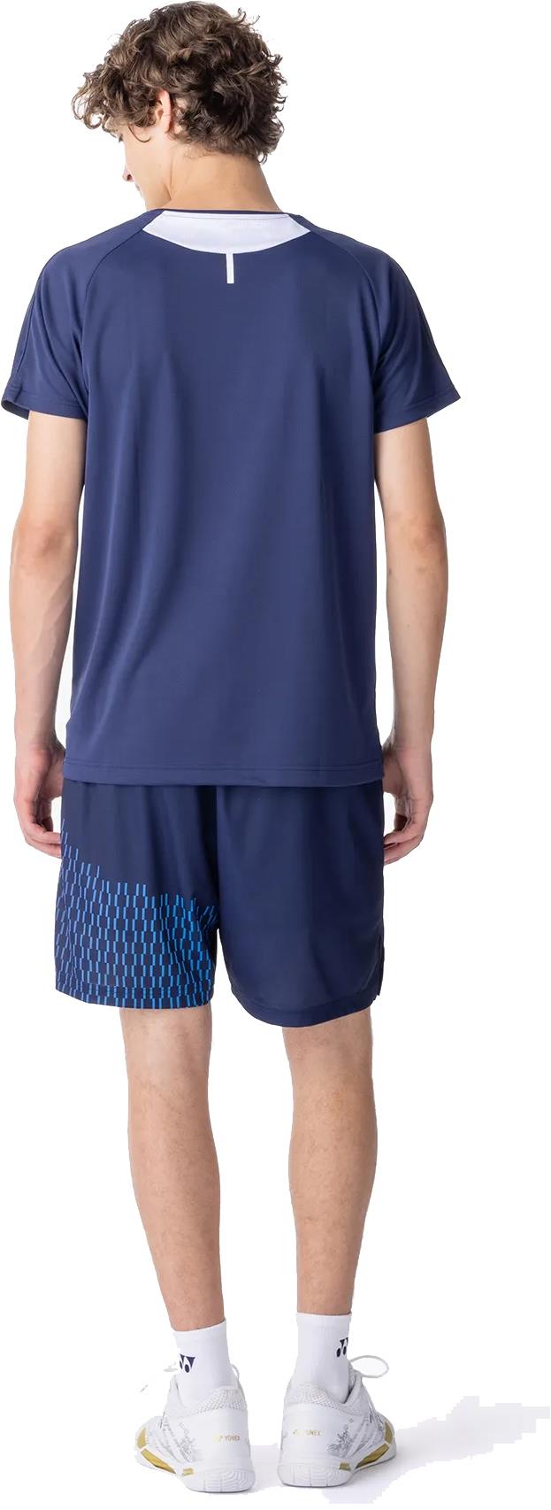 A young man faces away from the camera, wearing the Yonex 10713EX Crew Neck Men's Badminton T-Shirt in dark navy and matching shorts, both designed for moisture management, along with white socks and athletic shoes.