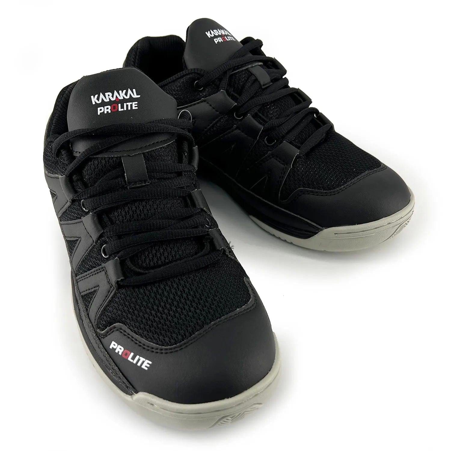 A pair of Karakal KF Pro Lite Badminton Shoes in the new black color is displayed, showcasing white branding, black laces, and gray soles. These shoes feature a mesh design on the upper for enhanced breathability and include a shock-absorbing gel insole for superior comfort. Additionally, they offer excellent lateral stability to support dynamic movements.