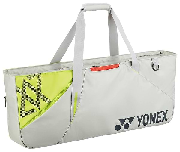 The Yonex 52531VA Viktor Axelsen Club Tournament Badminton Bag in Greyish Beige features white handles, a zippered top, neon yellow mesh pocket, and Yonex logo on the front. Perfect for carrying sports equipment and rackets.