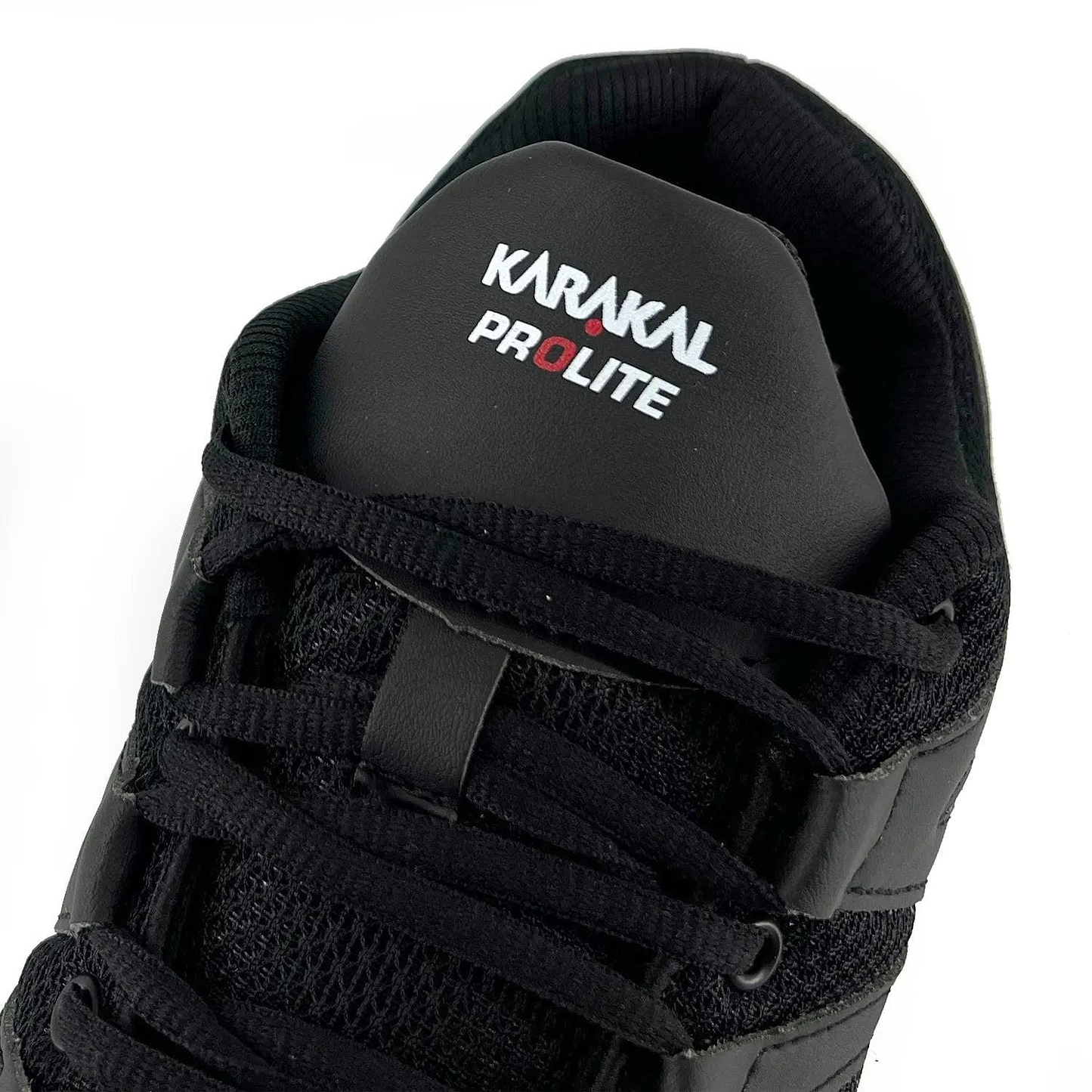 Close-up of a black Karakal KF Pro Lite Badminton Shoe, featuring the brand logo on the tongue. Ideal for badminton enthusiasts, this shoe boasts a textured mesh design with lace-up closure and lateral stability, complemented by a shock-absorbing gel insole for superior comfort and performance.