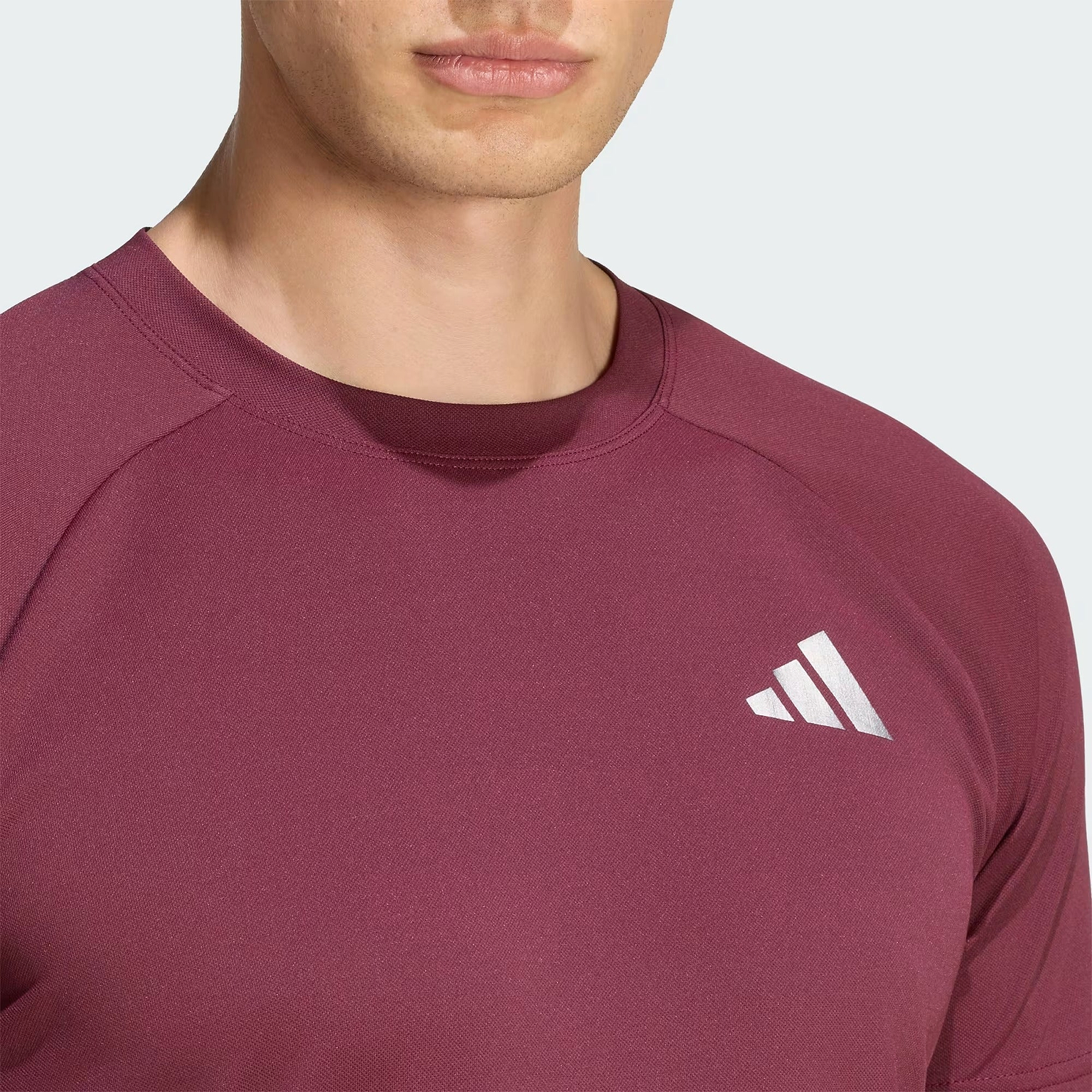 A person wearing the adidas Climacool+ Freelift Pro Men’s Badminton T-Shirt in maroon, featuring a white adidas logo on the chest, is shown from the shoulders up against a plain background.