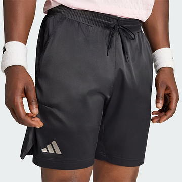 A person is wearing black adidas Climacool Ergo Pro Men’s Badminton Shorts, featuring an ergonomic cut, along with a light pink shirt and white wristbands. Only their lower torso and upper legs are visible as they stand with their hands by their sides.