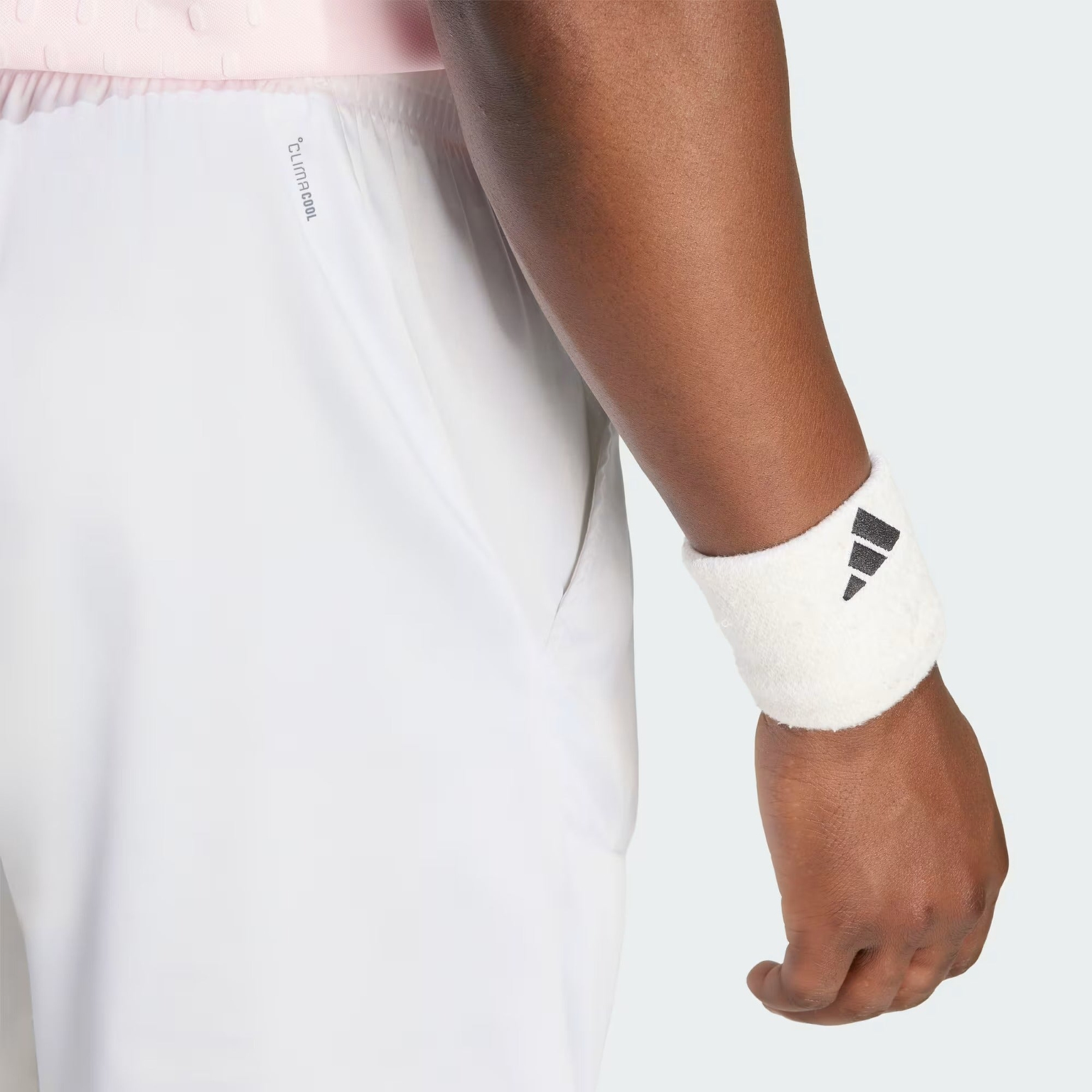 A person wearing adidas Climacool Ergo Pro Men’s Badminton Shorts in white and a white adidas wristband stands with their arm relaxed by their side against a plain background.