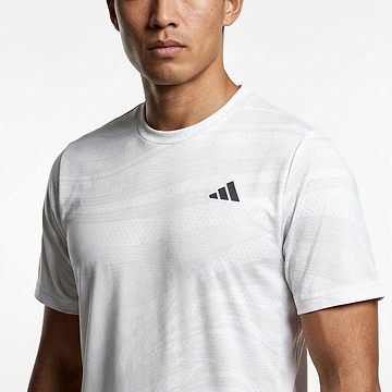 A man wears the adidas Mens Club Graphic Badminton T-Shirt in white/grey, a fitted short-sleeve sportswear top made from recycled materials with moisture-wicking fabric and a small black adidas logo on the chest.