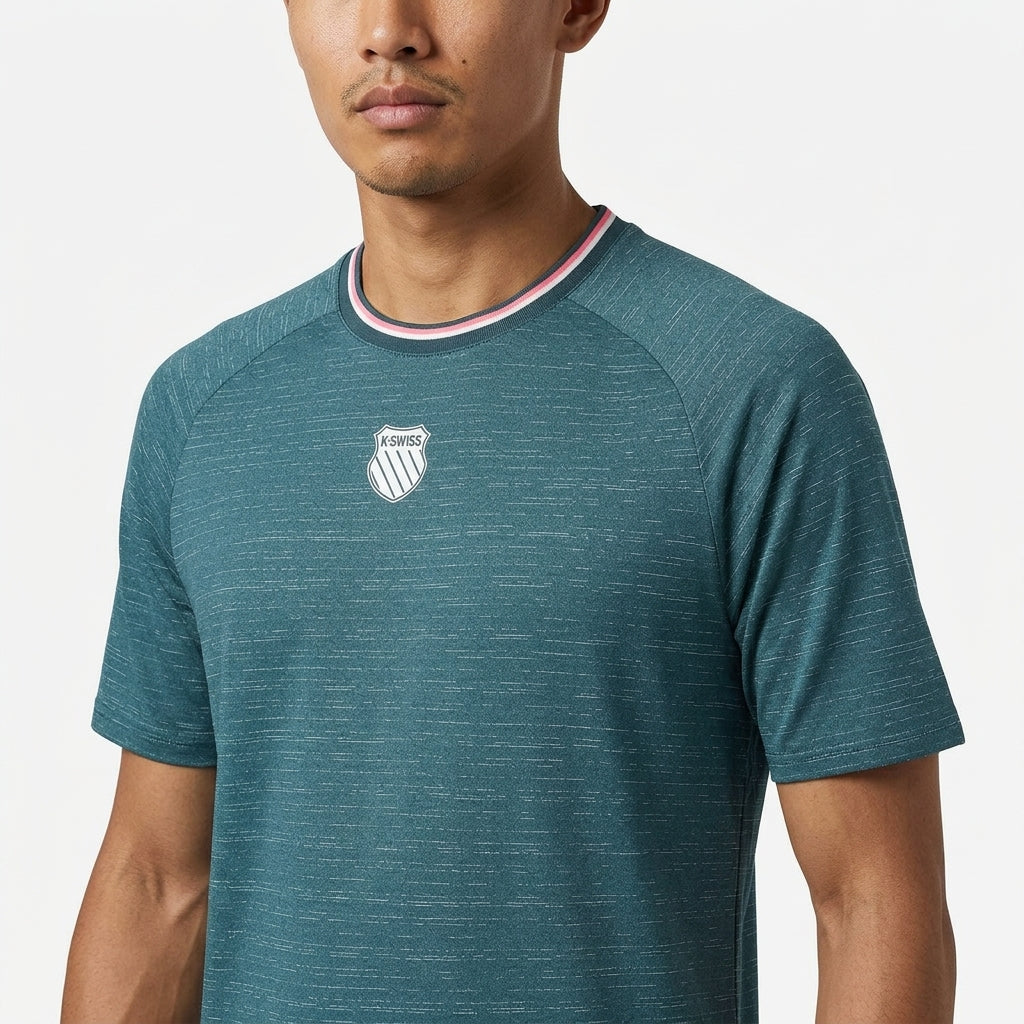 A man wears the K-Swiss Hypercourt Mens Melange 3 Badminton T-Shirt in Stargazer—a teal performance tee with a small white chest logo and a collar featuring red, white, and blue stripes—standing against a plain white background.