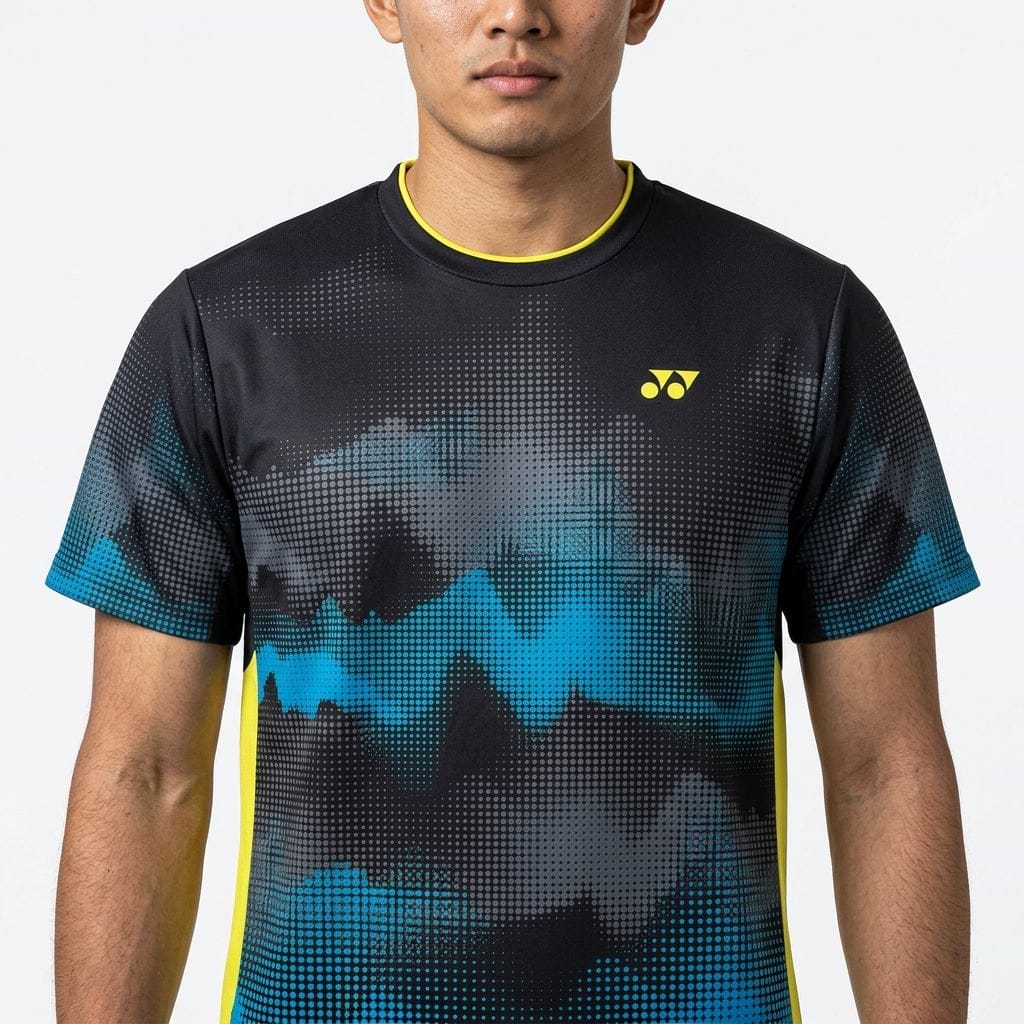 A man faces forward wearing the Yonex YTM2025A Men's Badminton T-Shirt in black, featuring an abstract black and blue design, yellow Yonex logo, quick-dry technology, and yellow trim on the collar and sides. Only his upper body is visible.