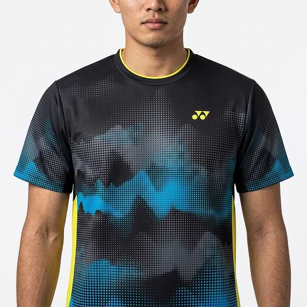 A man faces forward wearing the Yonex YTM2025A Men's Badminton T-Shirt in black, featuring an abstract black and blue design, yellow Yonex logo, quick-dry technology, and yellow trim on the collar and sides. Only his upper body is visible.