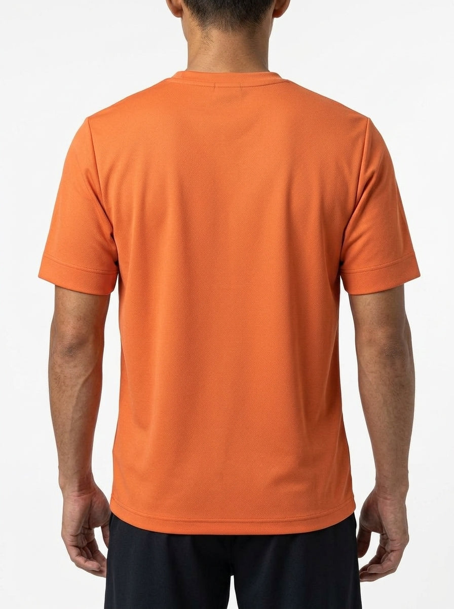 A person with their back to the camera wears a bright orange HEAD Slice II Men's Badminton T-Shirt - CN by HEAD, made of moisture transfer microfiber, and black shorts, standing against a plain white background.