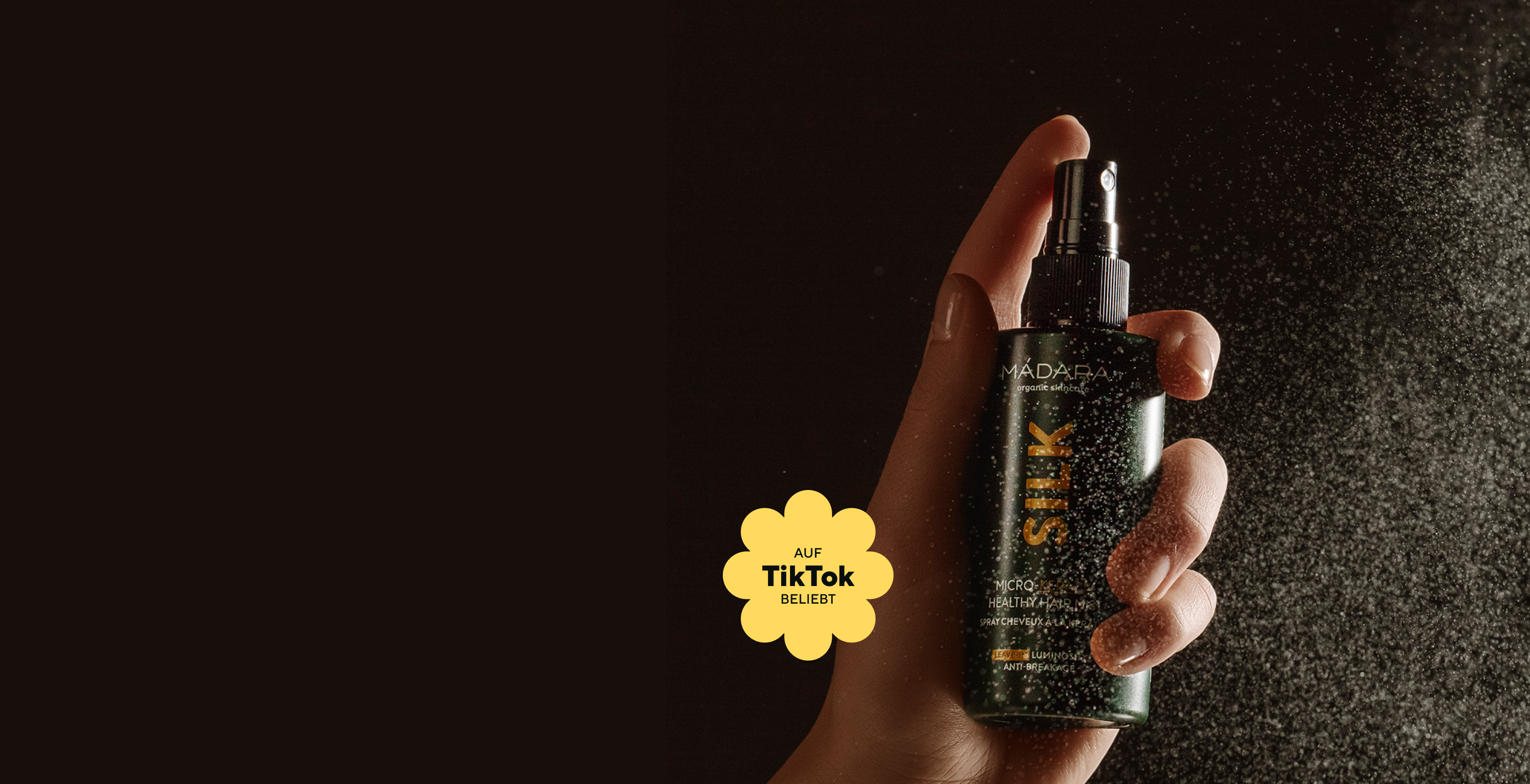 Hand spraying MÁDARA Silk micro-keratin hair mist against a dark background with visible mist particles