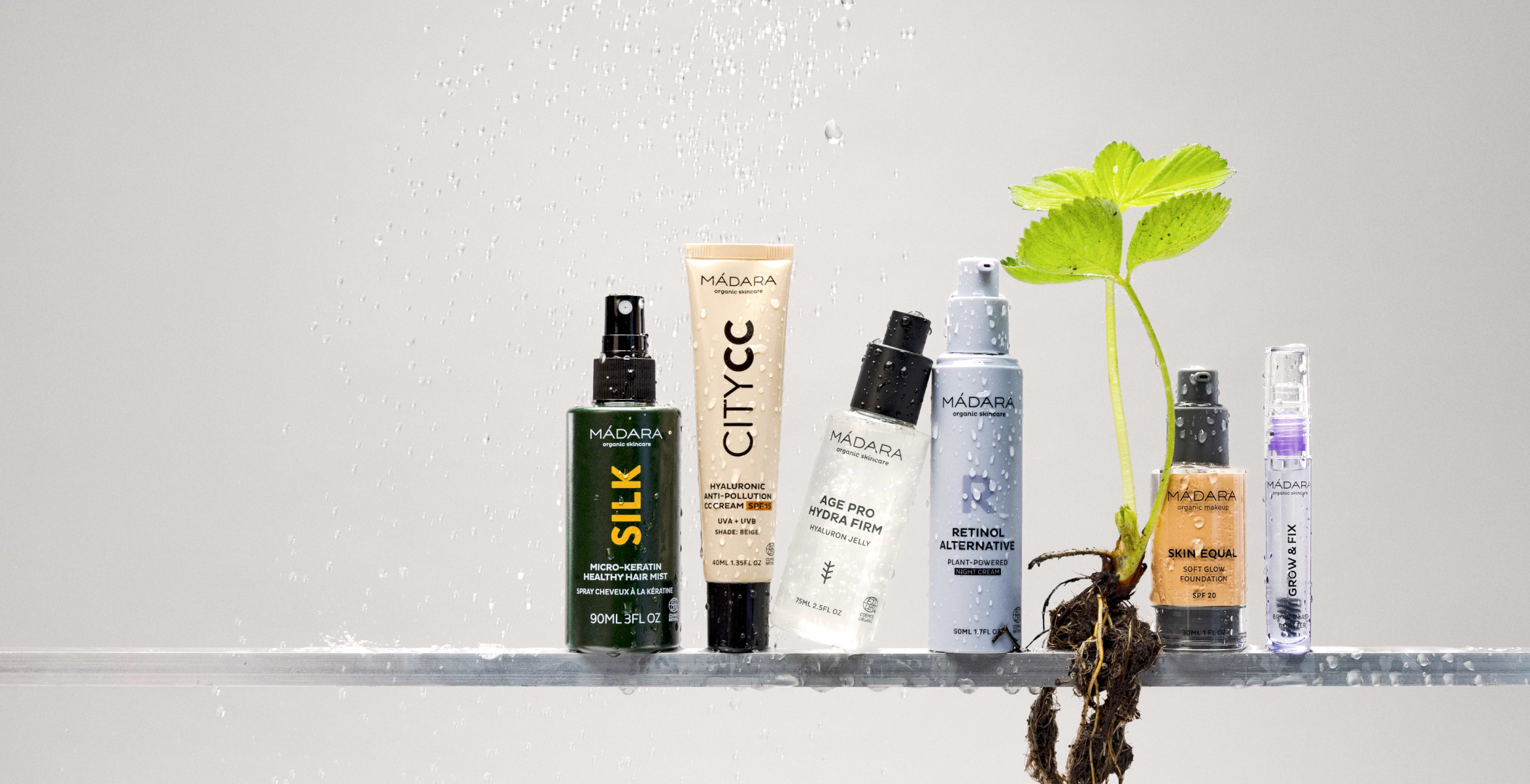 Full MÁDARA beauty routine with hair mist, CC cream, serum, retinol alternative and foundation displayed with water splash and botanical roots symbolizing natural care