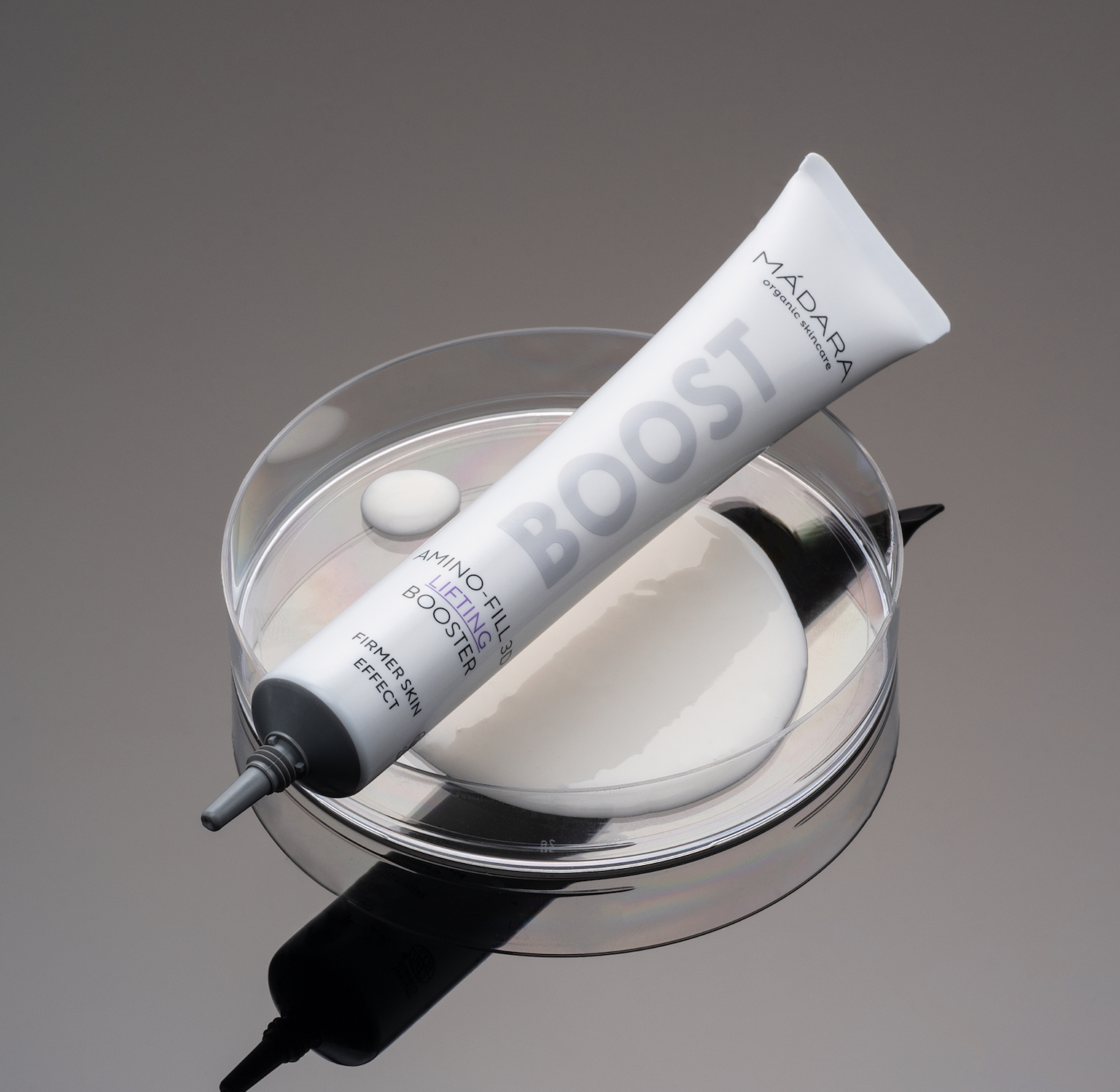 MÁDARA BOOST Amino-Fill 3D Lifting Booster tube displayed on a laboratory petri dish with skincare formula, highlighting a science-inspired approach to firming and lifting skincare