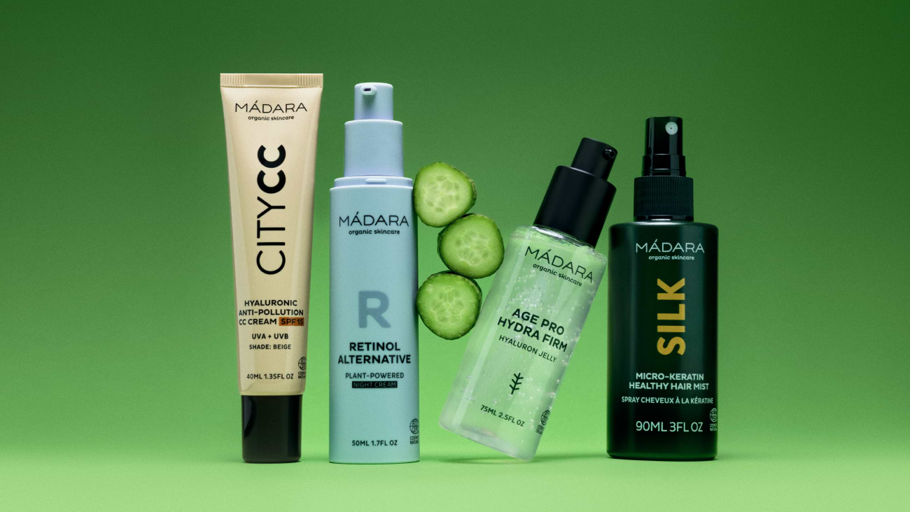 MÁDARA skincare products including City CC cream, retinol alternative, Hydra Firm serum and hair mist on green background with fresh cucumber slices