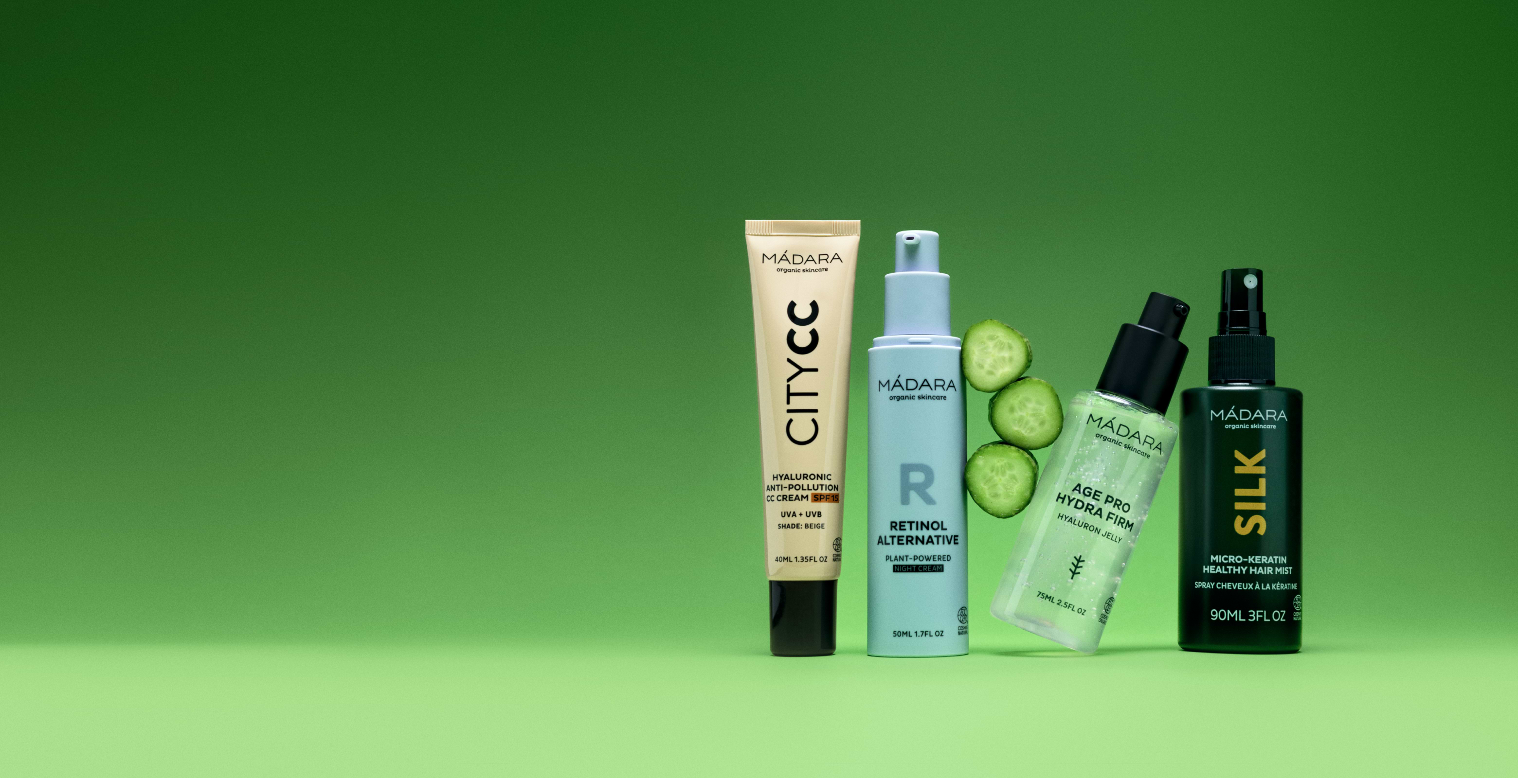 MÁDARA skincare products including City CC cream, retinol alternative, Hydra Firm serum and hair mist on green background with fresh cucumber slices homepage banner