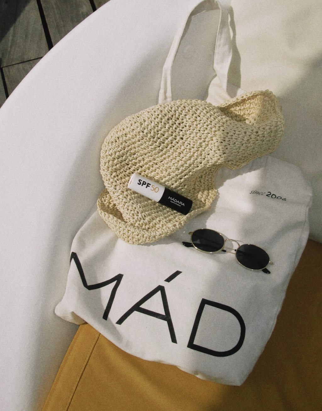 Sun hat, SPF 50 sunscreen, and sunglasses on a white tote bag in warm sunlight