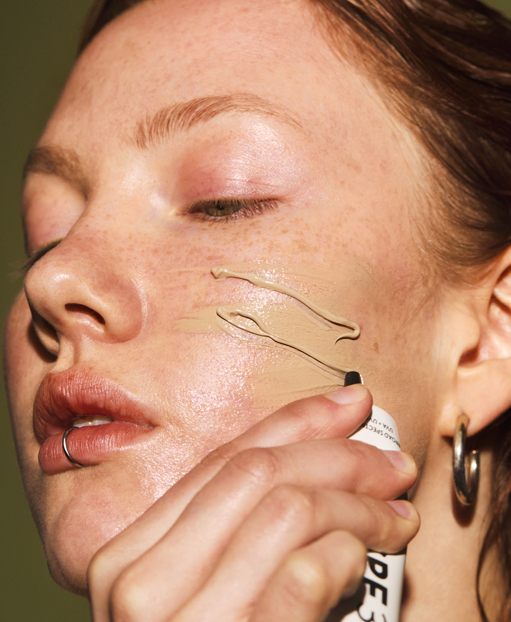 Primer plano de una mujer aplicándose el protector solar mineral orgánico con SPF 30 de Madara en la mejilla, en el que se aprecia la textura cremosa y el acabado radiante sobre la piel natural