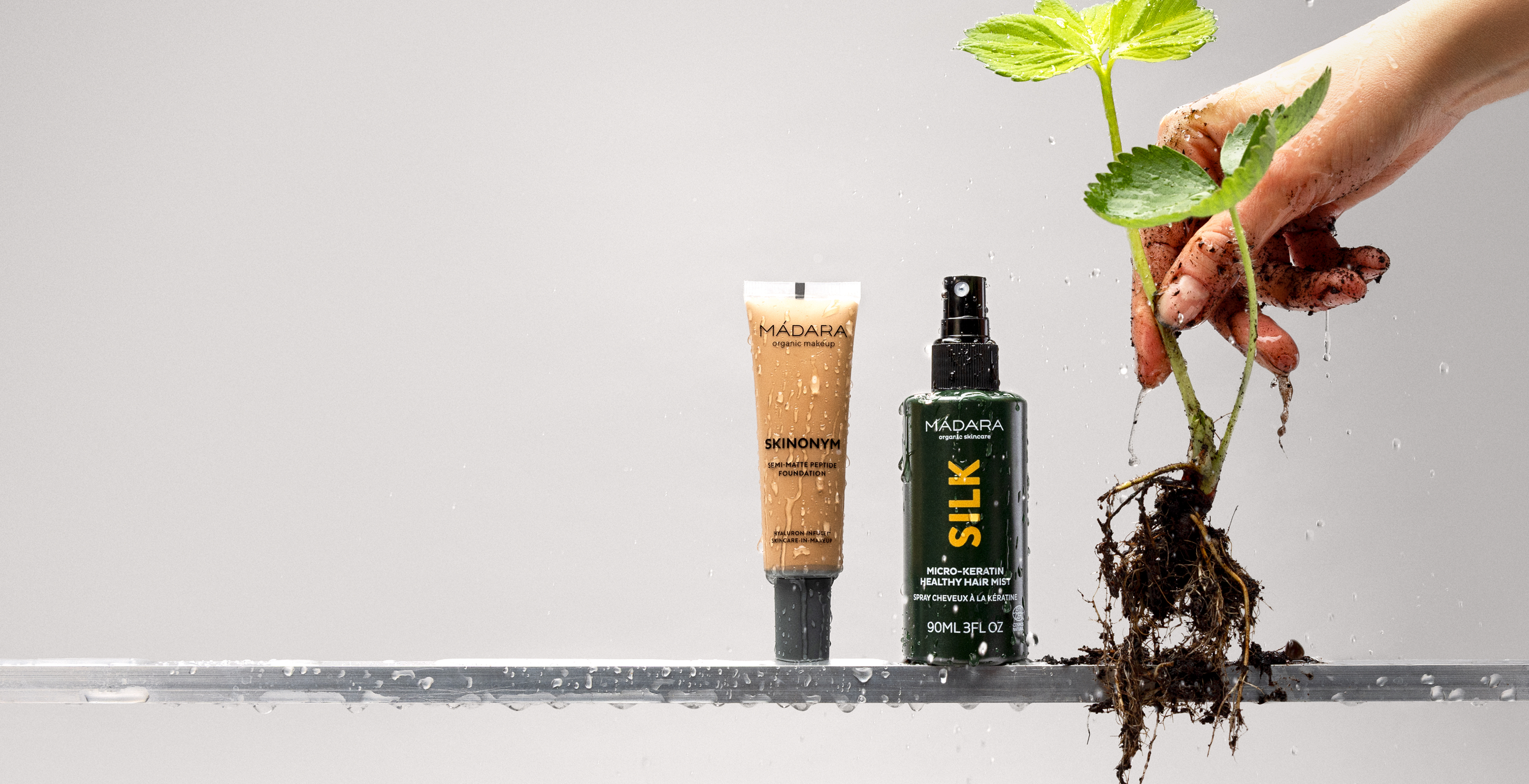 secret sale homepage banner with MÁDARA Skinonym foundation and Silk hair mist displayed with a freshly pulled plant and water droplets