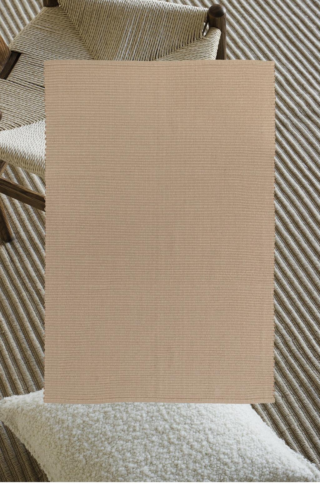 Beige textured wool rug shown draped over a natural fibre chair