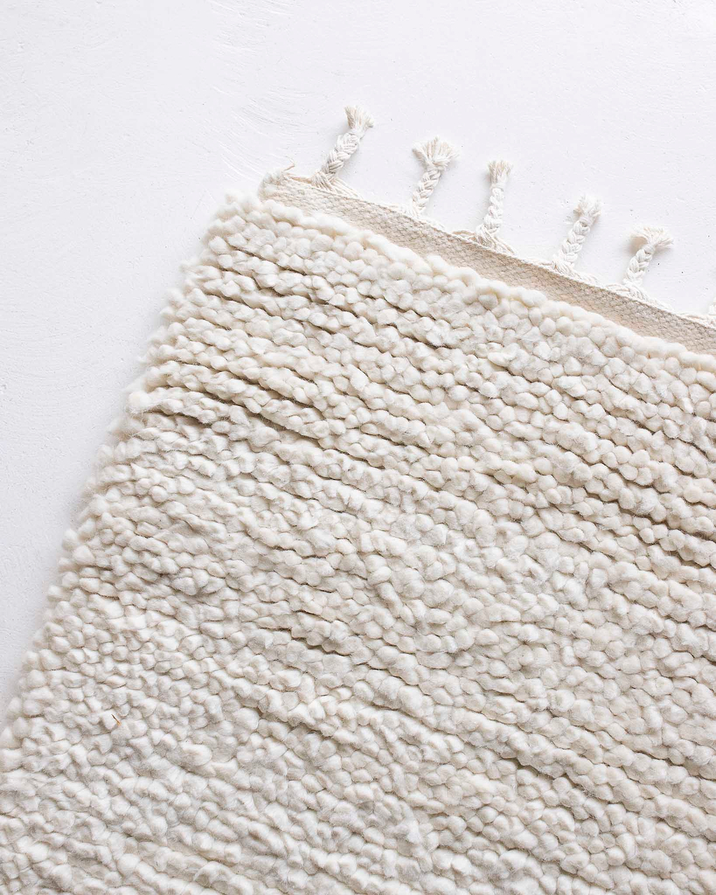 Close-up of a textured white ivory rug with fringe on a light background by Rugs for Good. 