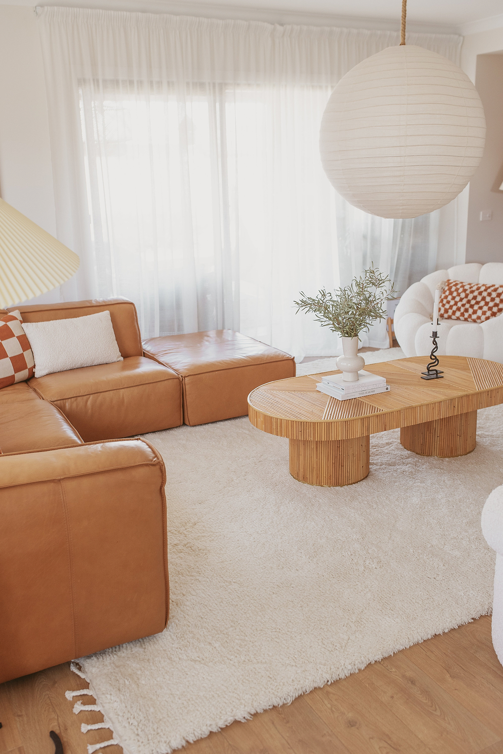 A white wool rug with a subtle diamond pattern, placed in a living room setting under a round hanging lamp, with a brown leather sofa and wooden table in the background.