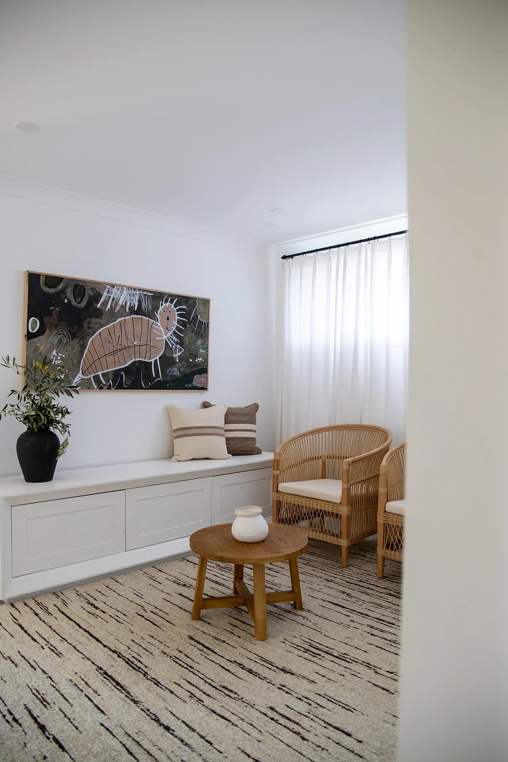 Modern living room with wicker chair and wooden coffee table on a wool rug from Rugs for Good, with abstract art on the wall.