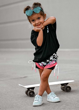 Girl child standing on a skateboard wearing a Little Trouble black