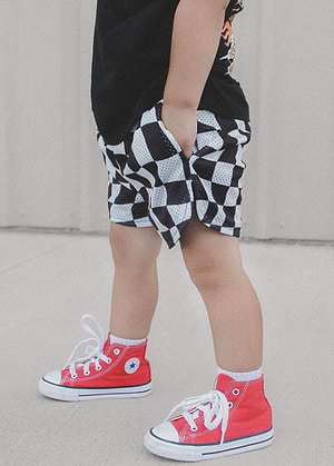 Child wearing Little Trouble black and white checkered basketball shorts with red high-top sneakers on a neutral background
